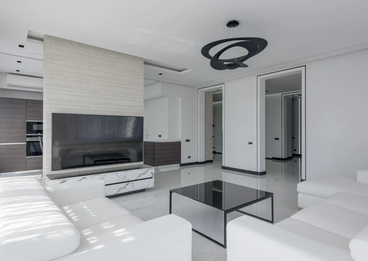 Modern bright house interior with table and sofa near TV with cabinet and white walls near entrance and lamp in Littleton