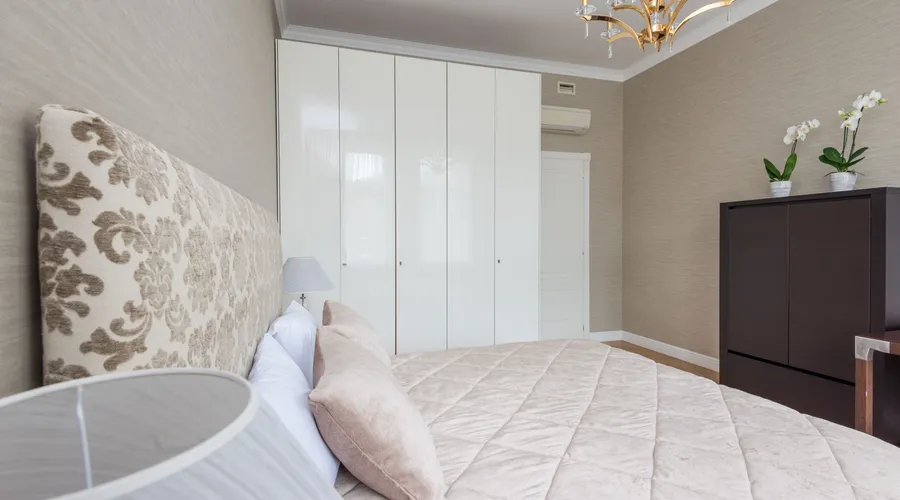 Behr Dynasty - Bed under coverlet with cushions placed near lamp on bedside and closet near door in bedroom with classic chandelier